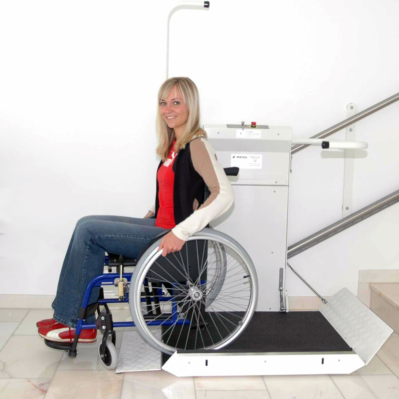 Dame im Rollstuhl benutzt einen Plattformlift um eine Treppe zu überwinden.